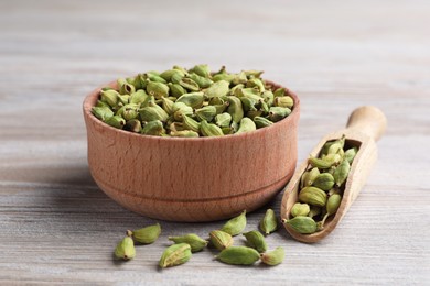 Bowl and scoop with dry cardamom pods on wooden table, closeup