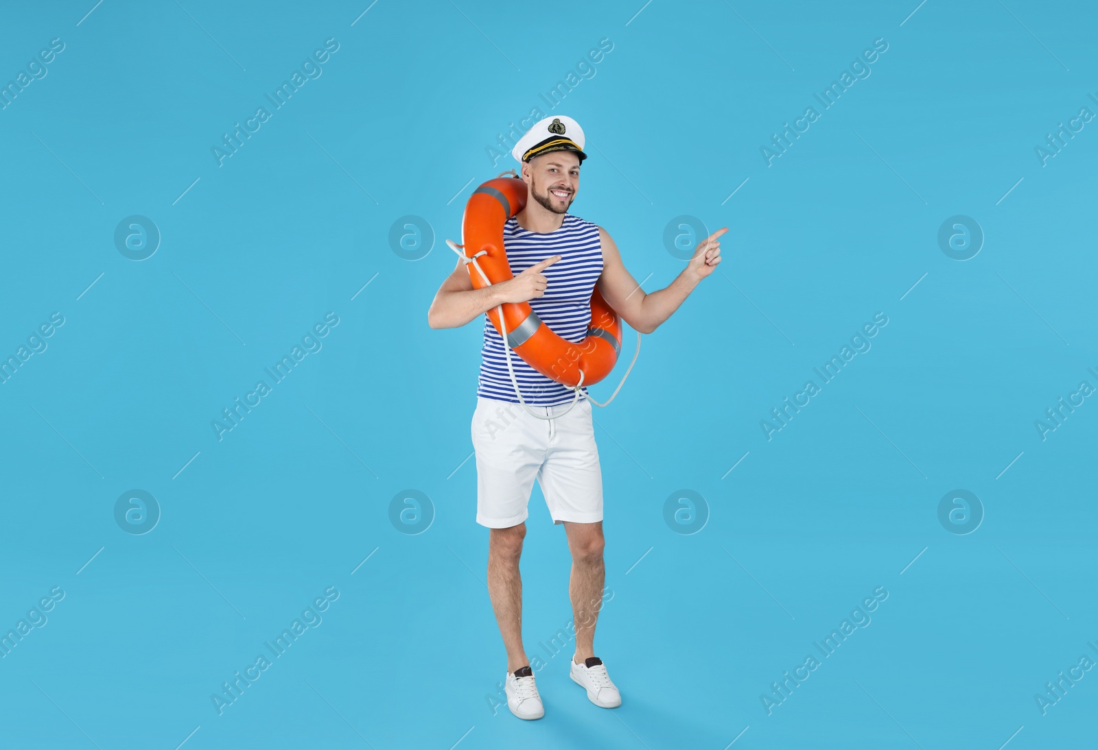 Photo of Happy sailor with orange ring buoy pointing on light blue background
