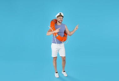 Photo of Happy sailor with orange ring buoy pointing on light blue background