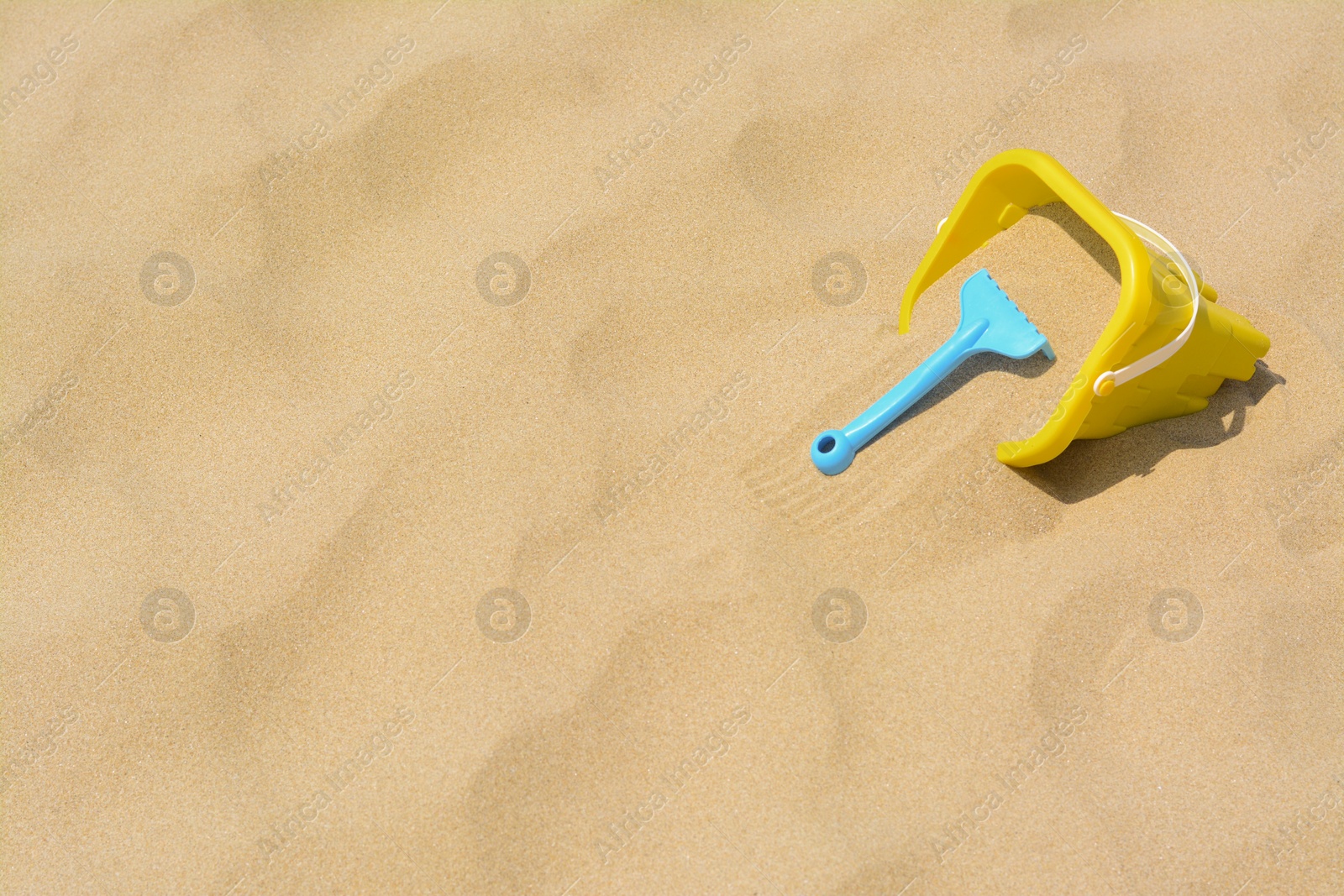 Photo of Plastic bucket and rake on sand, space for text. Beach toys