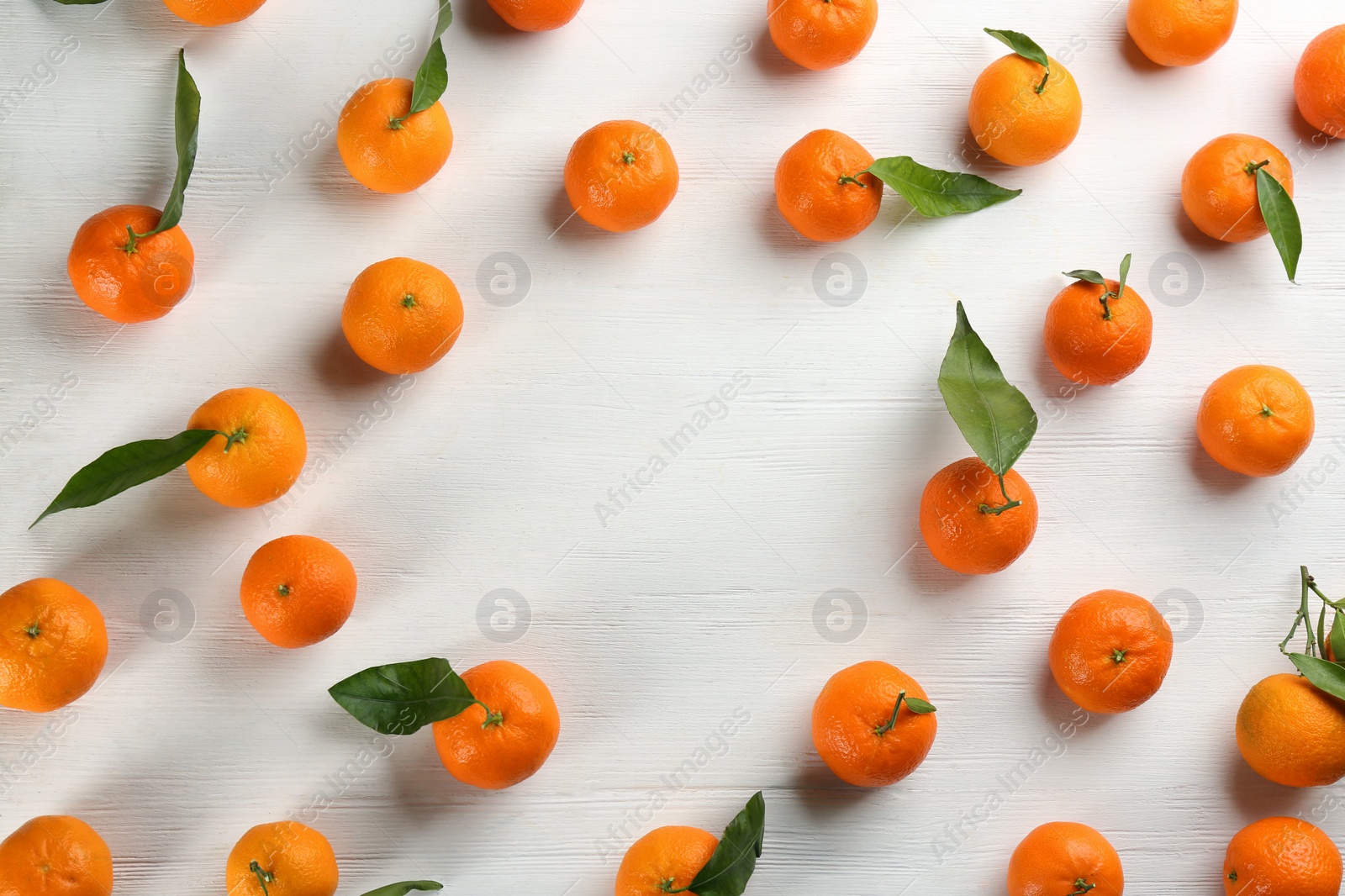 Photo of Fresh ripe tangerines with green leaves on white wooden table, flat lay. Space for text