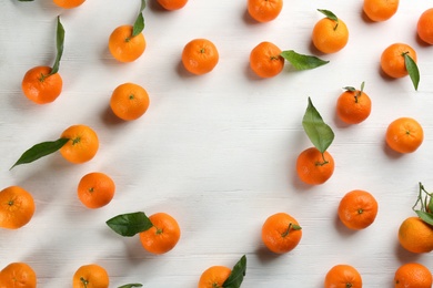 Fresh ripe tangerines with green leaves on white wooden table, flat lay. Space for text