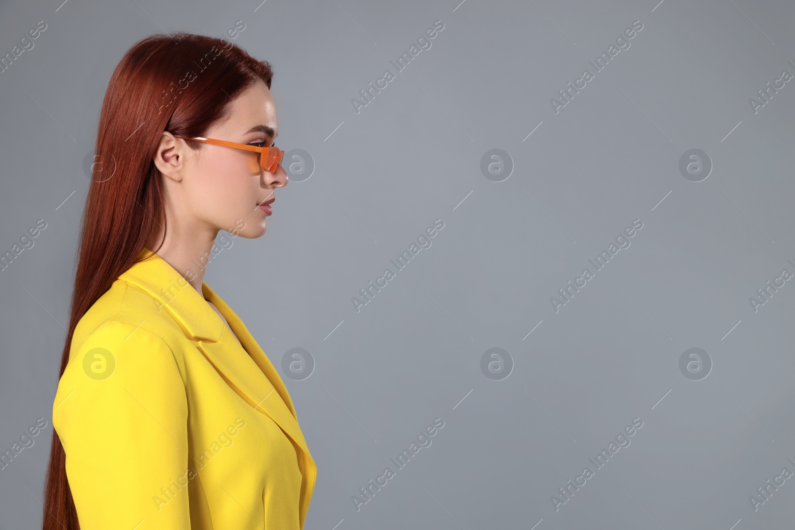 Photo of Stylish woman with red dyed hair and orange sunglasses on light gray background, space for text