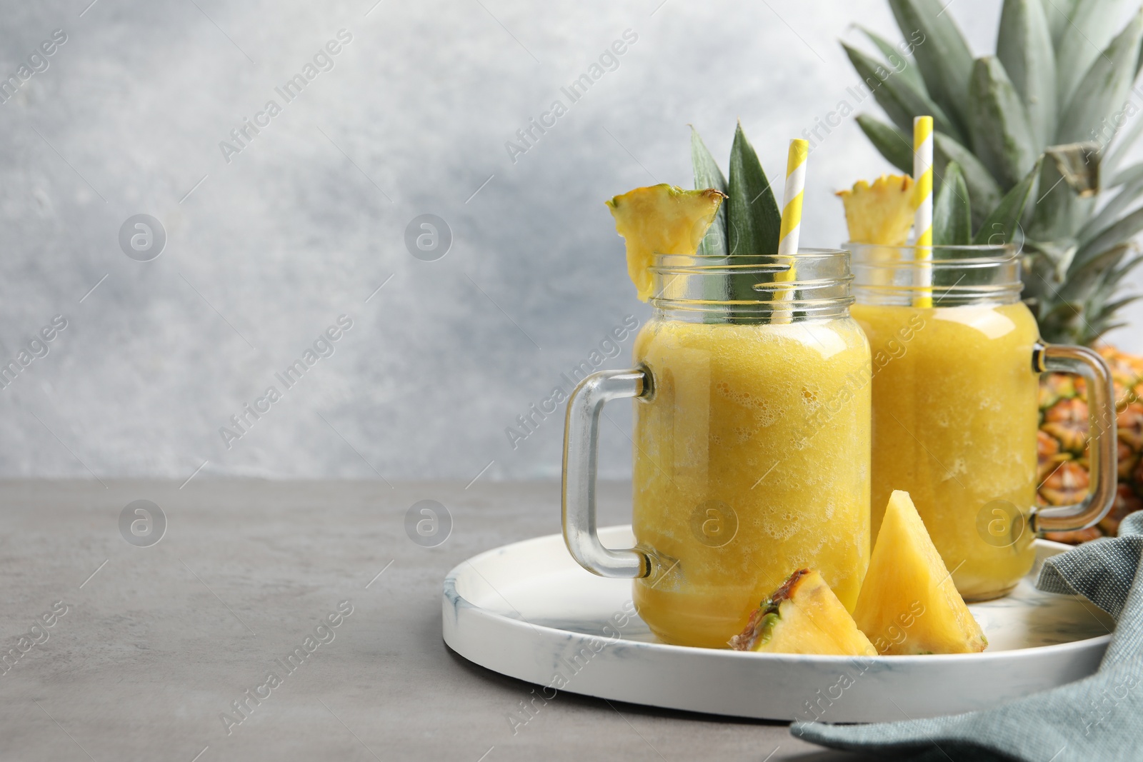 Photo of Tasty pineapple smoothie and sliced fruit on grey table. Space for text