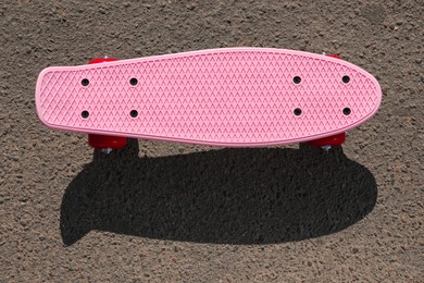 Photo of Modern pink skateboard with red wheels on asphalt road outdoors, top view