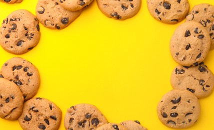 Photo of Frame made of many delicious chocolate chip cookies on yellow background, flat lay. Space for text