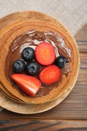 Photo of Tasty pancakes with chocolate paste and berries on wooden table, top view