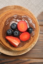 Tasty pancakes with chocolate paste and berries on wooden table, top view