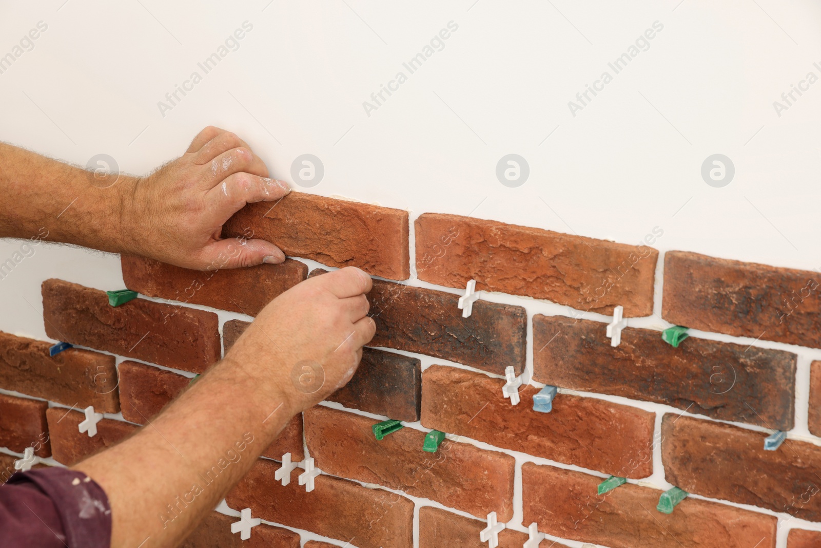 Photo of Professional builder installing new brown decorative bricks on wall, closeup