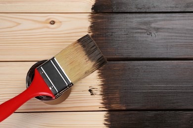 Photo of Brush and can of wood stain on wooden surface, top view