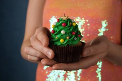 Photo of Woman holding tasty Christmas cupcake on blue background, closeup