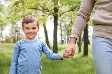 Photo of Happy little child holding hands with his father in park. Family time