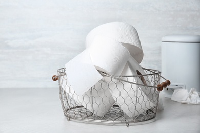 Photo of Basket with toilet paper rolls on floor indoors. Personal hygiene