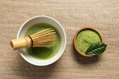 Photo of Cup of fresh matcha tea with bamboo whisk and green powder on wooden table, flat lay