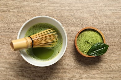 Cup of fresh matcha tea with bamboo whisk and green powder on wooden table, flat lay