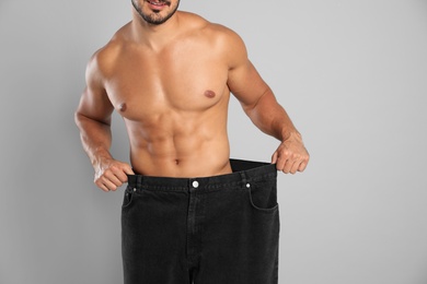 Young man with slim body in old big size jeans on grey background, closeup view