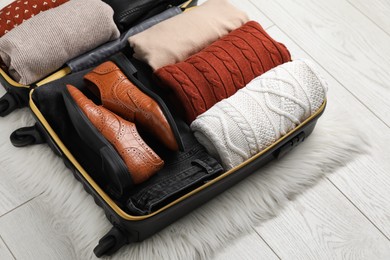 Photo of Open suitcase with folded clothes, shoes and accessories on floor