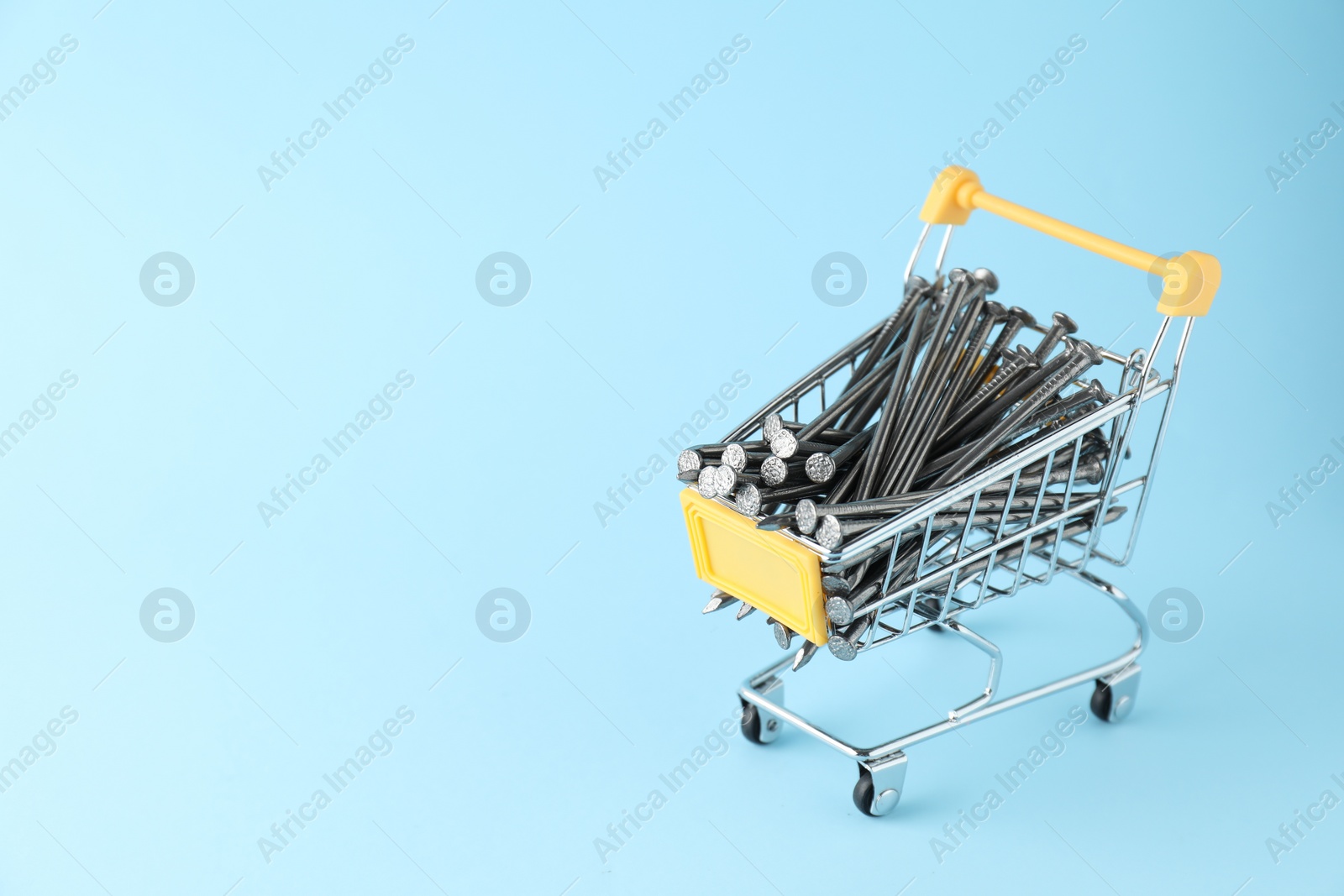 Photo of Metal nails in shopping cart on light blue background, space for text