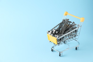 Photo of Metal nails in shopping cart on light blue background, space for text