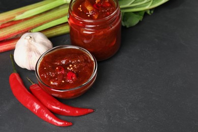 Photo of Tasty rhubarb sauce and ingredients on black table, space for text