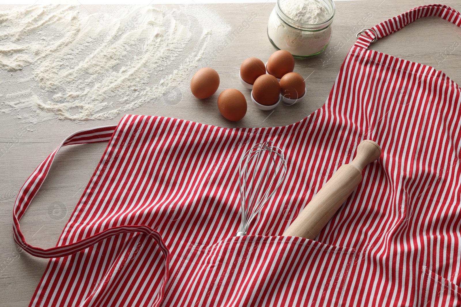 Photo of Red striped apron with kitchen tools and different ingredients on wooden table