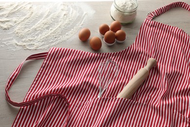Red striped apron with kitchen tools and different ingredients on wooden table