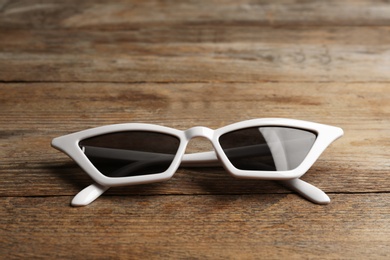 Photo of Stylish sunglasses on wooden background. Fashionable accessory