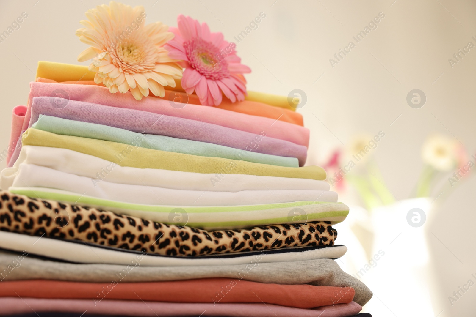 Photo of Stack of clean clothes and flowers on blurred background, closeup