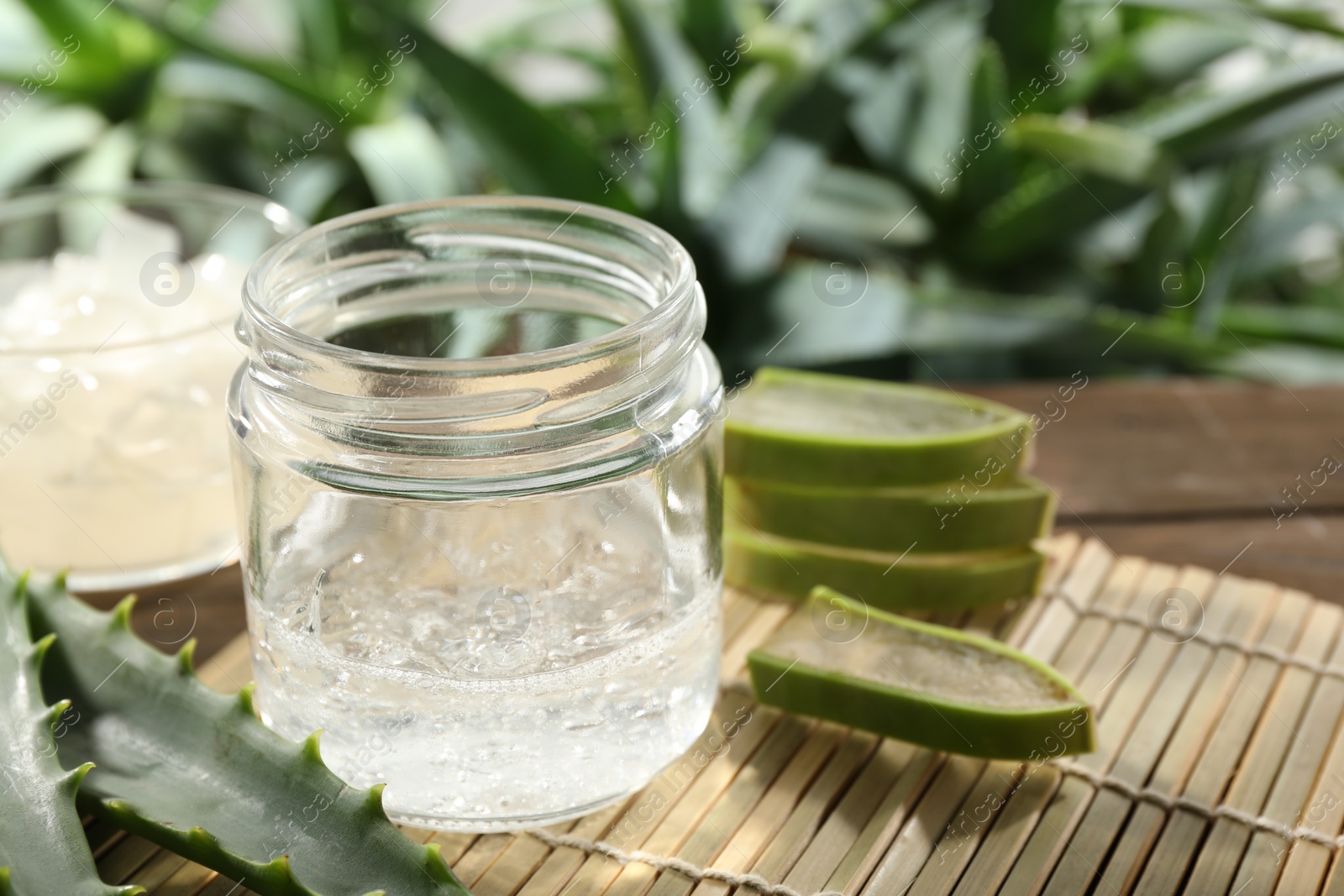 Photo of Aloe vera gel in jar and slices of plant on bamboo mat, closeup