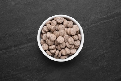 Photo of Brewer's yeast tablets in bowl on black table, top view