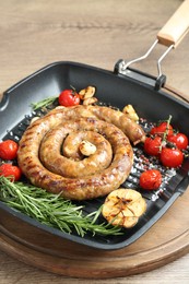 Delicious homemade sausage with garlic, tomatoes, rosemary and spices in grill pan on wooden table, closeup