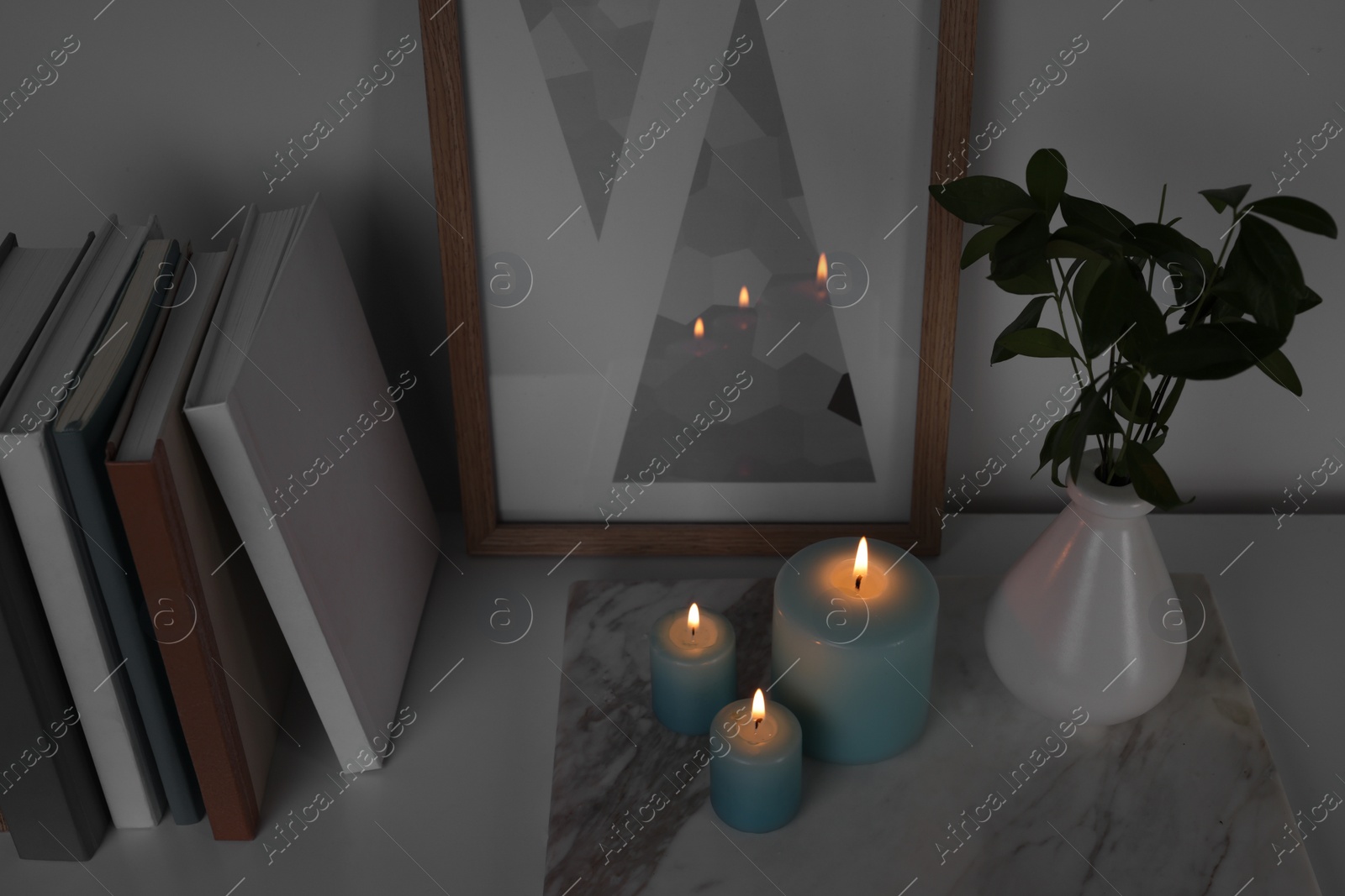 Photo of Burning candles, books, picture and vase with green branches on white table