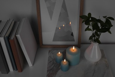 Burning candles, books, picture and vase with green branches on white table