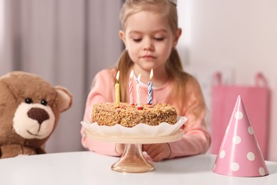 Cute girl with birthday cake at table indoors, focus on burning candles