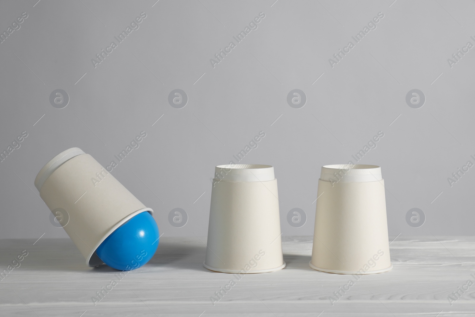 Photo of Shell game. Three paper cups and ball on white wooden table
