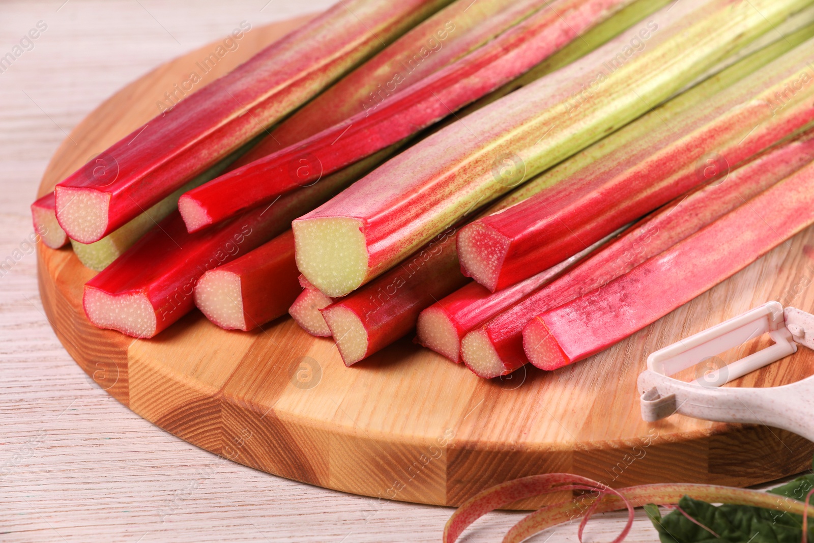 Photo of Cut fresh rhubarb stalks and peeler on white wooden table, closeup