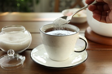 Photo of Woman adding sugar into aromatic tea at wooden table indoors, closeup