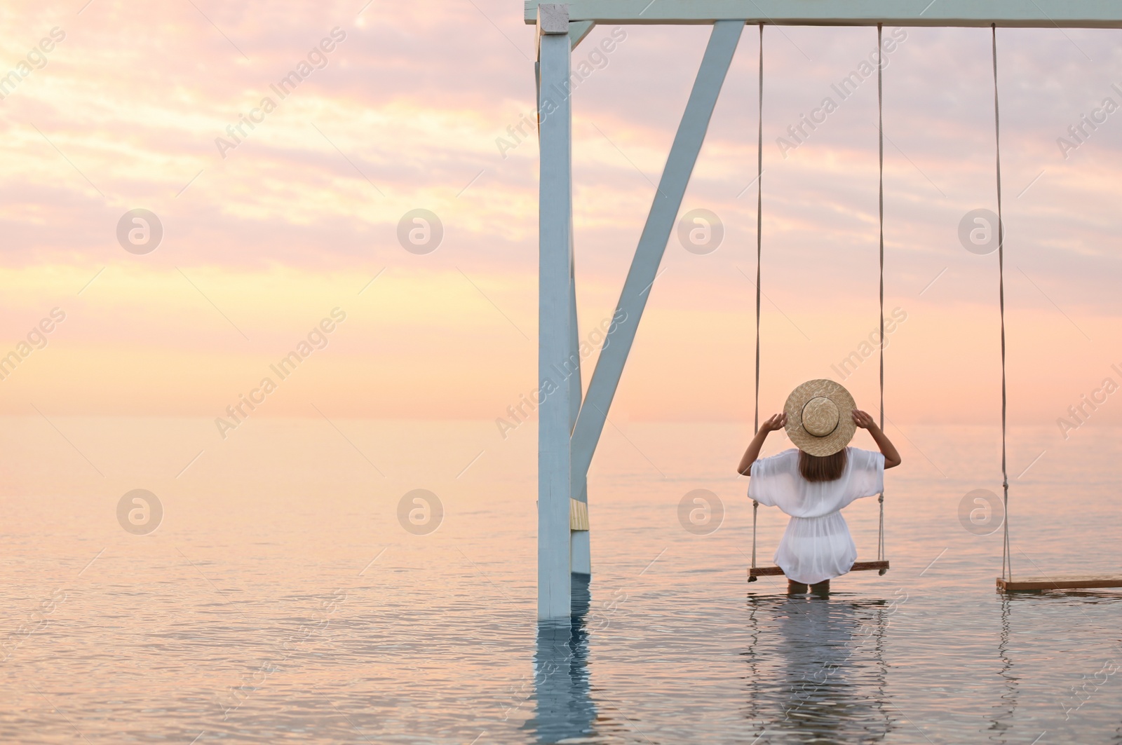 Photo of Young woman enjoying sunrise on swing over water