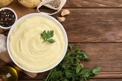 Photo of Bowl of tasty mashed potato, parsley, garlic, olive oil and pepper on wooden table, flat lay. Space for text