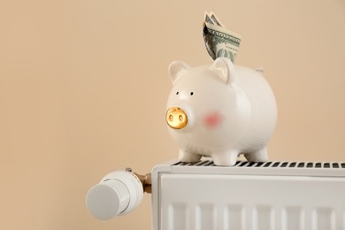 Piggy bank with money on heating radiator against light background
