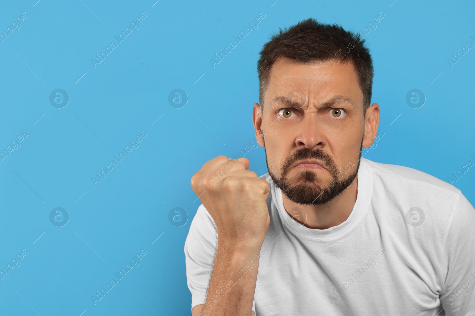 Photo of Aggressive man on light blue background, space for text