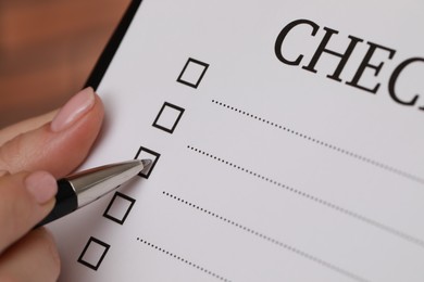 Photo of Woman filling Checklist with pen, closeup view