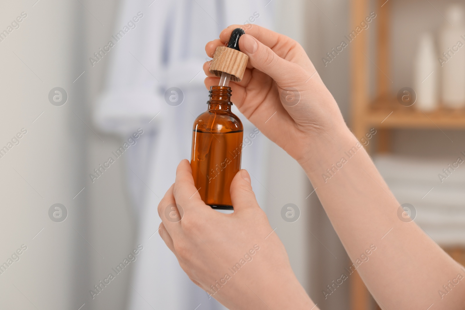 Photo of Woman with bottle of essential oil in bathroom, closeup