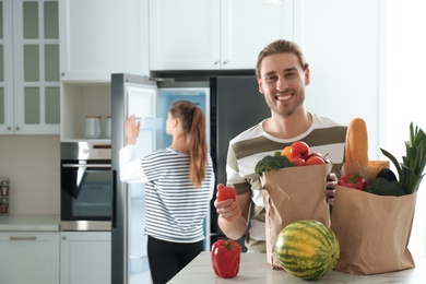 Photo of Man with fresh products at table and woman near refrigerator in kitchen