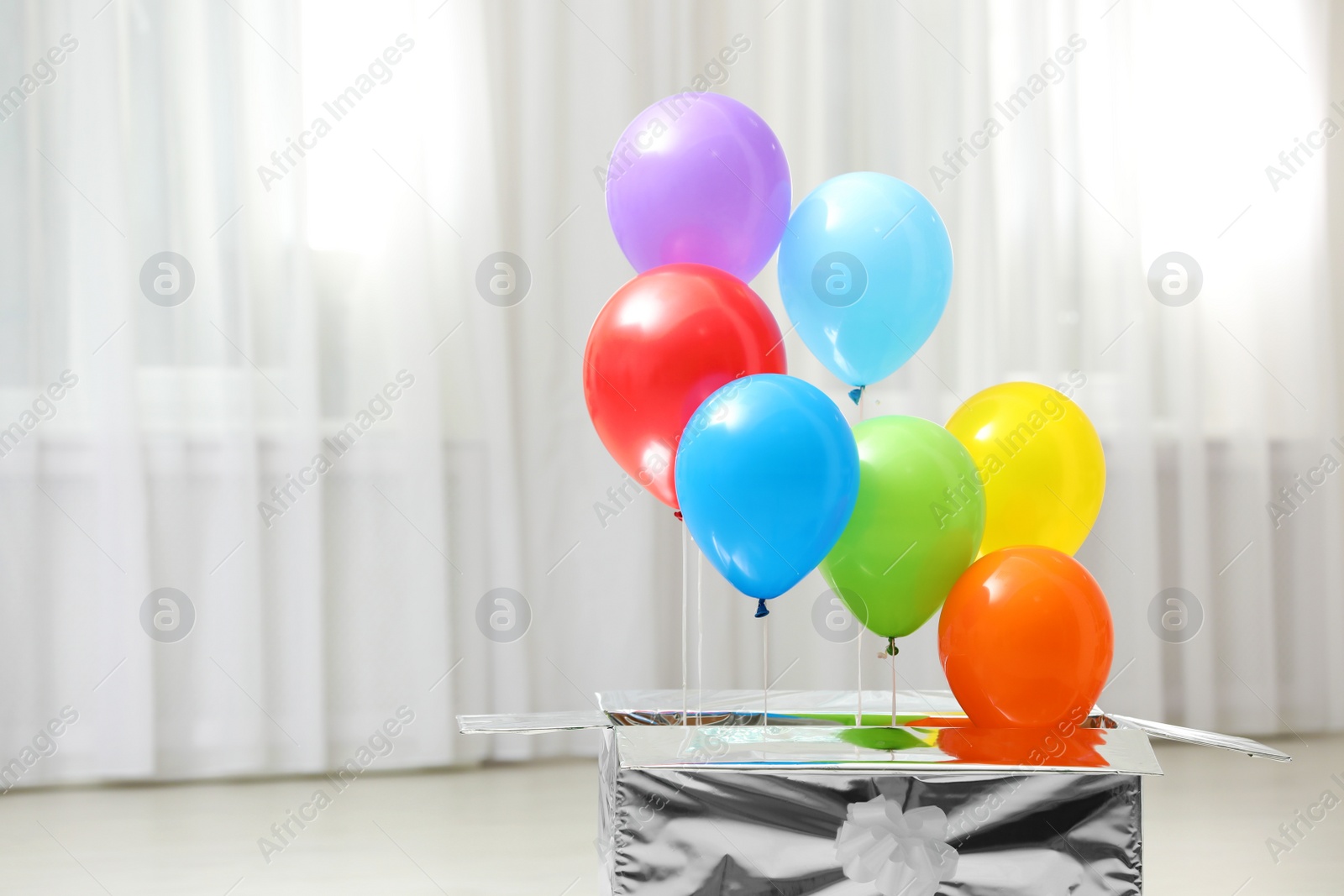 Photo of Gift box with bright air balloons indoors. Space for text