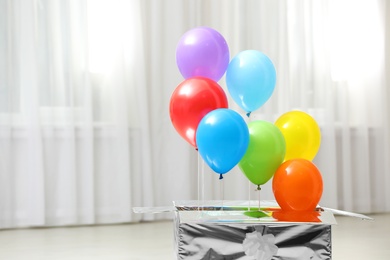 Gift box with bright air balloons indoors. Space for text