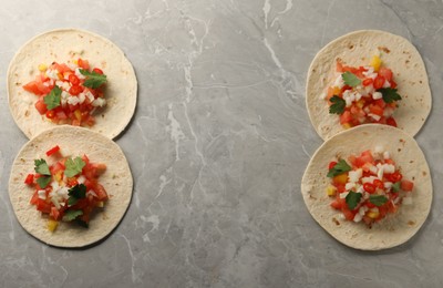 Delicious tacos with vegetables and parsley on grey marble table, top view. Space for text