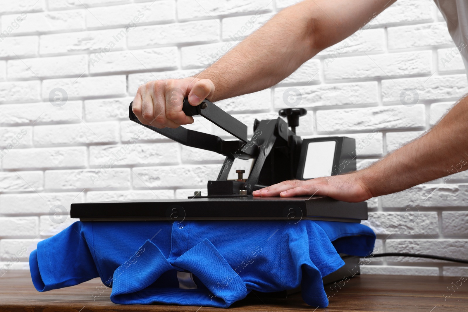 Photo of Man using heat press machine at table near white brick wall, closeup