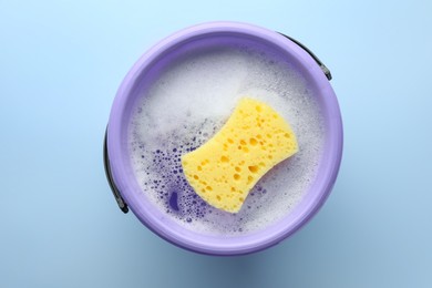Photo of Bucket with foam and sponge on light blue background, top view