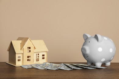 Piggy bank, dollar banknotes and house model on wooden table against beige background